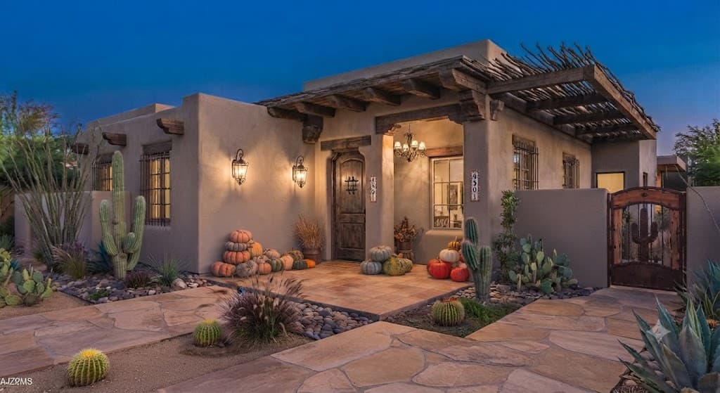 Southwestern-style home with a wooden pergola and pumpkin piles by the front door